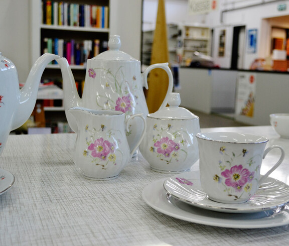 Weißes Kaffeegeschirr mit einer rosa Blume steht auf einem weißen Tisch. 