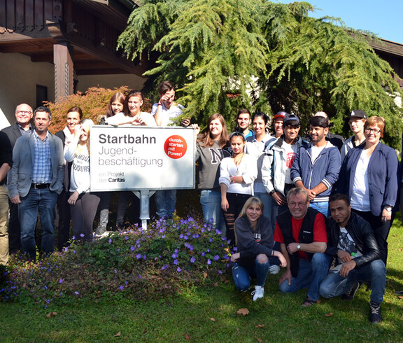 Ein Gruppenfoto vor einem Haus im Grünen. Mehrere Mädchen halten ein Schild mit der Aufschrift: Startbahn Jugendbeschäftigung in der Hand. 